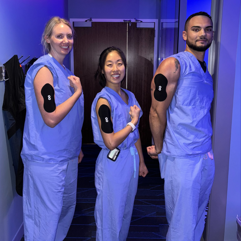 Three people in blue scrubs showing adhesive patches on their upper arms.