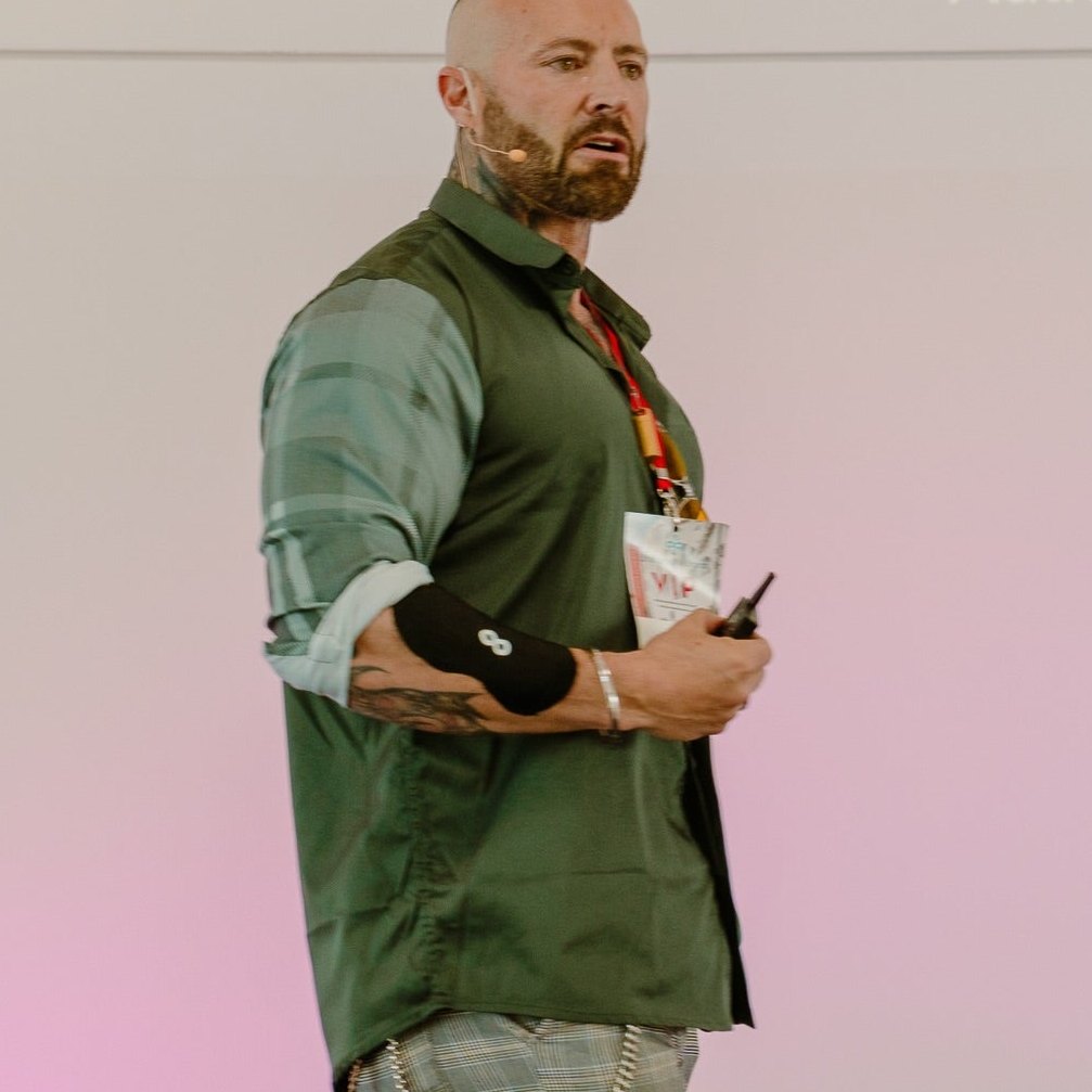 Coach Kris Gethin speaking on stage wearing an Ion Layer NAD+ patch