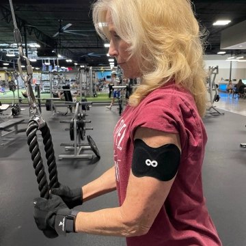 Woman using a cable machine in a gym, wearing an Ion Layer patch on her upper arm.